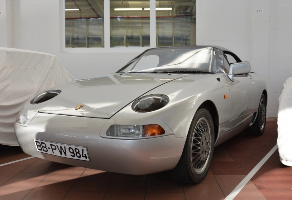 White Porsche sports prototype car with pop-up headlights displayed in an indoor showroom or garage space