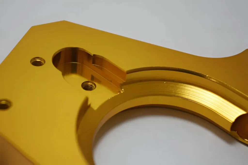 A close-up view of a metal part with a golden anodized finish. The surface looks smooth and vibrant.