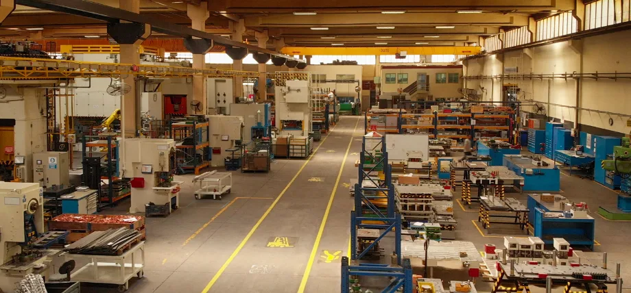 Spacious manufacturing facility with multiple CNC machines, workbenches, and overhead cranes in a well-organized low-volume production environment.