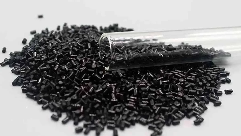 A pile of black plastic pellets next to a glass test tube