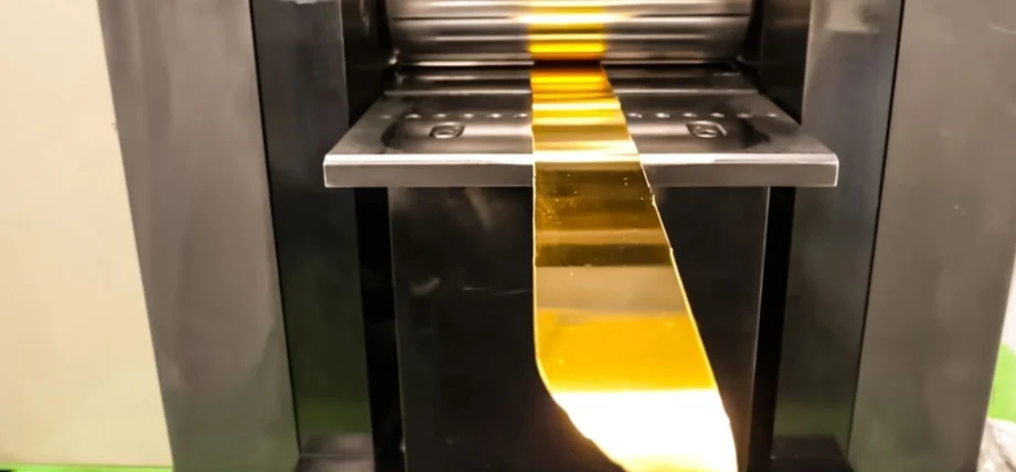 Industrial rolling mill compressing a thin gold sheet for uniform thickness in jewelry production.