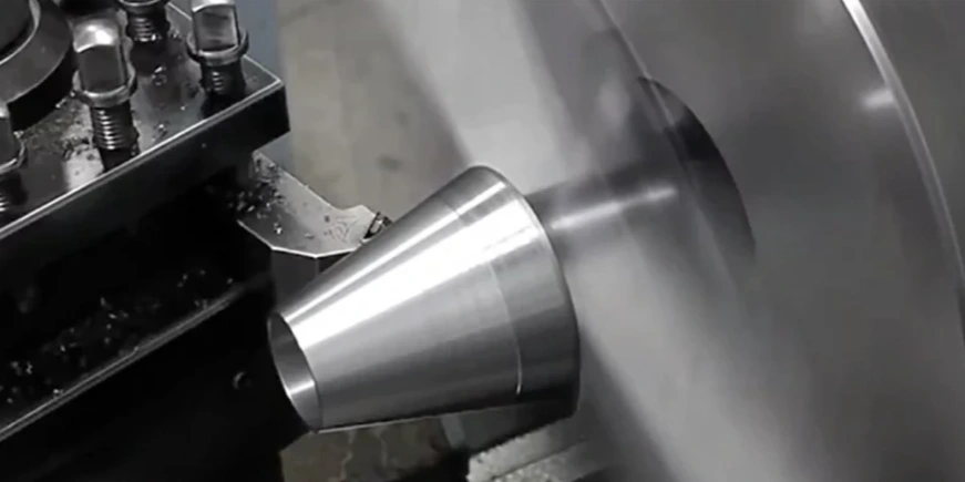 An image of taper turning showing a rotating tapered metal part being machined by a cutting tool