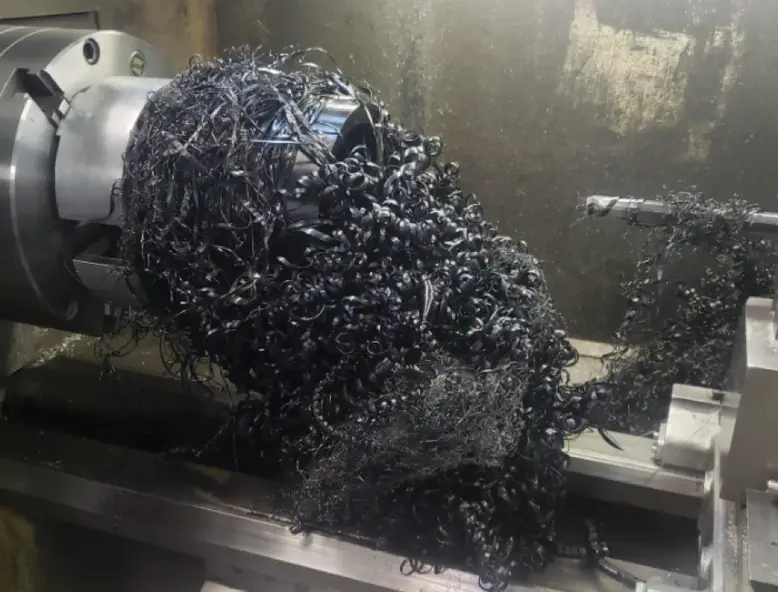 CNC lathe machining operation producing dark UHMW polyethylene chip swarf from a cylindrical workpiece held in a chuck 